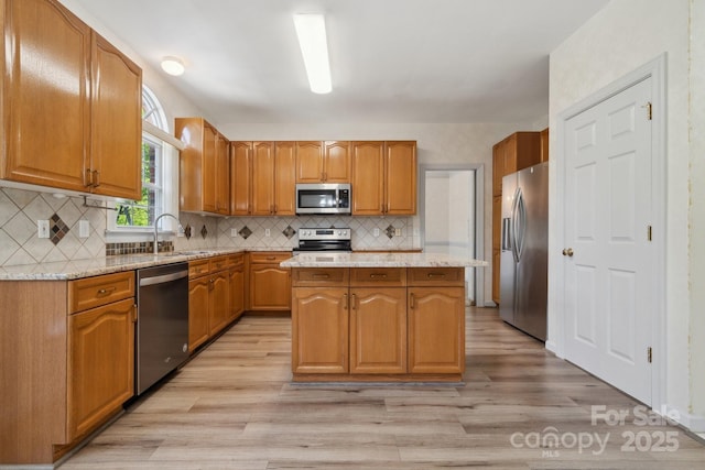 kitchen with a kitchen island, appliances with stainless steel finishes, a sink, light stone counters, and light wood-style floors