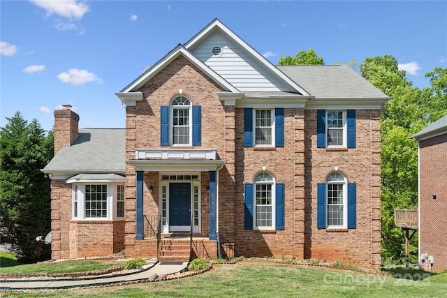 view of front facade featuring a chimney, a front yard, and brick siding