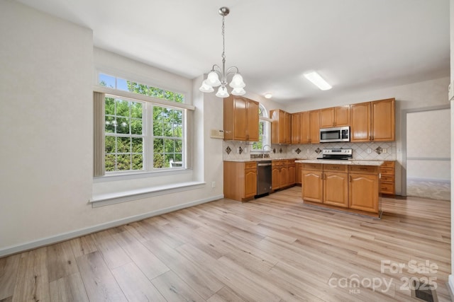 kitchen featuring a notable chandelier, light countertops, stainless steel appliances, light wood-type flooring, and backsplash