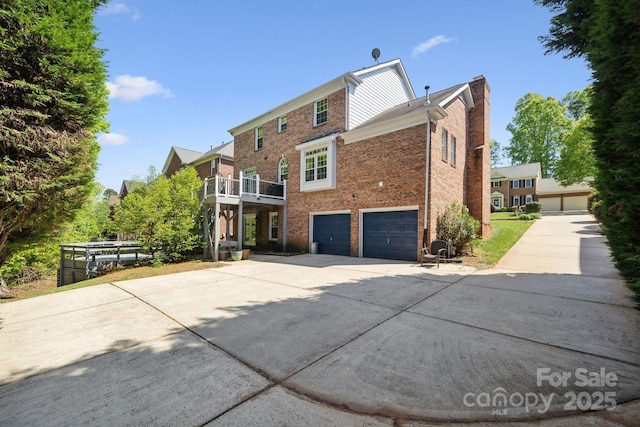 back of house featuring brick siding, an attached garage, a chimney, and concrete driveway