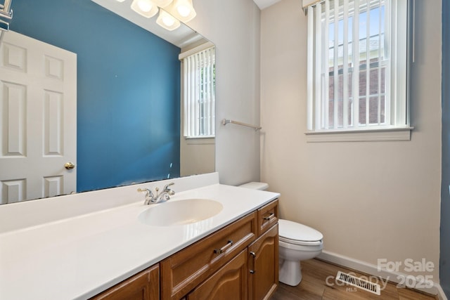 bathroom with visible vents, vanity, wood finished floors, toilet, and baseboards