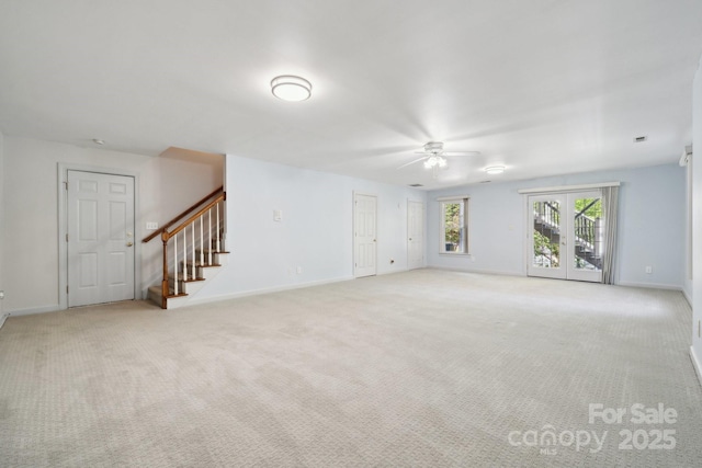 unfurnished living room featuring ceiling fan, light colored carpet, baseboards, and stairway