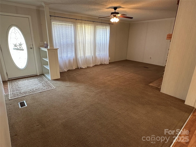 carpeted entrance foyer with visible vents, ornamental molding, a textured ceiling, and ceiling fan