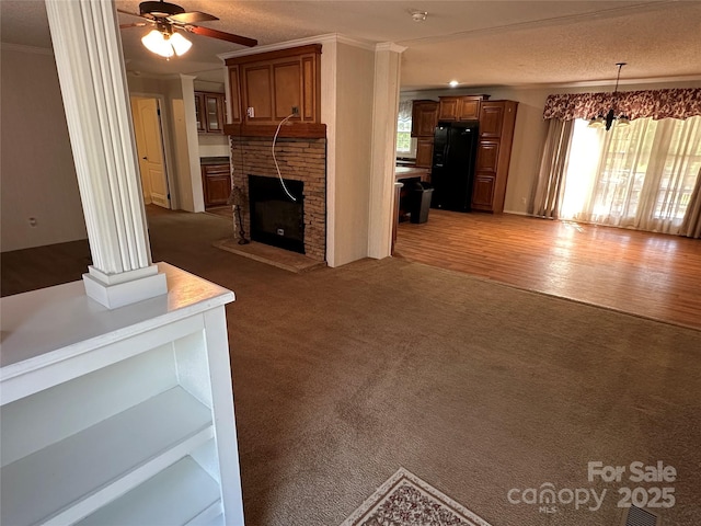 unfurnished living room featuring light colored carpet, ornamental molding, a brick fireplace, and a ceiling fan