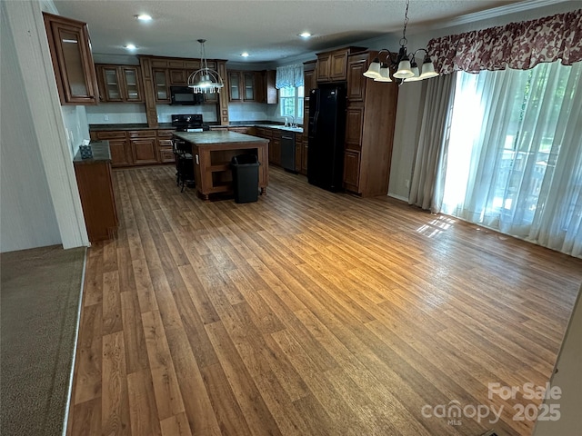 kitchen with wood finished floors, a kitchen island, a chandelier, a sink, and black appliances