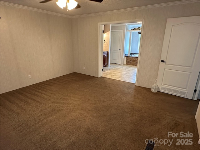 carpeted empty room with crown molding, ceiling fan, and visible vents