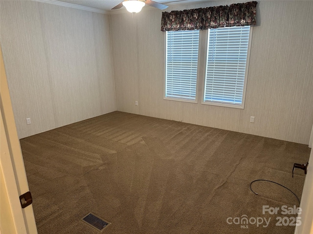 carpeted spare room with a ceiling fan, visible vents, and ornamental molding