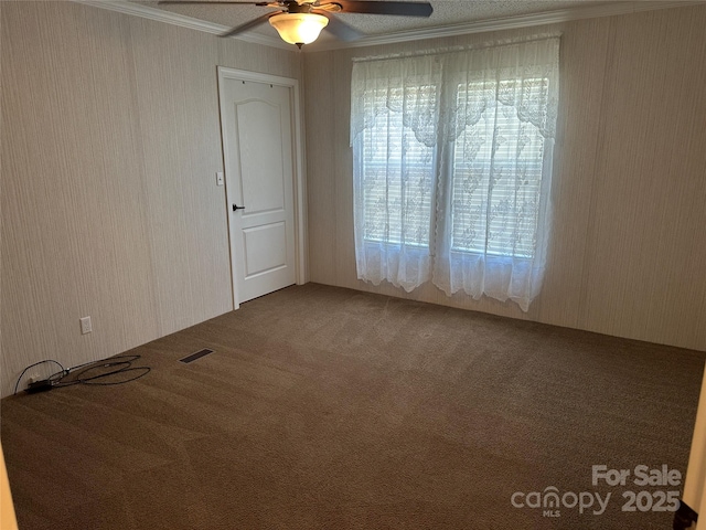 carpeted spare room featuring a ceiling fan, visible vents, and ornamental molding
