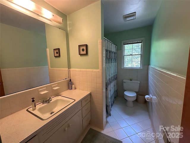 bathroom with tile patterned flooring, vanity, wainscoting, toilet, and tile walls