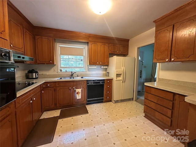 kitchen with a sink, light countertops, brown cabinetry, under cabinet range hood, and black appliances