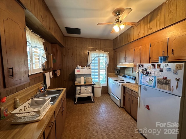 kitchen with white appliances, ceiling fan, wooden walls, under cabinet range hood, and a sink