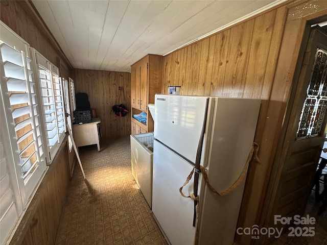 kitchen with freestanding refrigerator, washer / dryer, brown cabinets, and wood walls