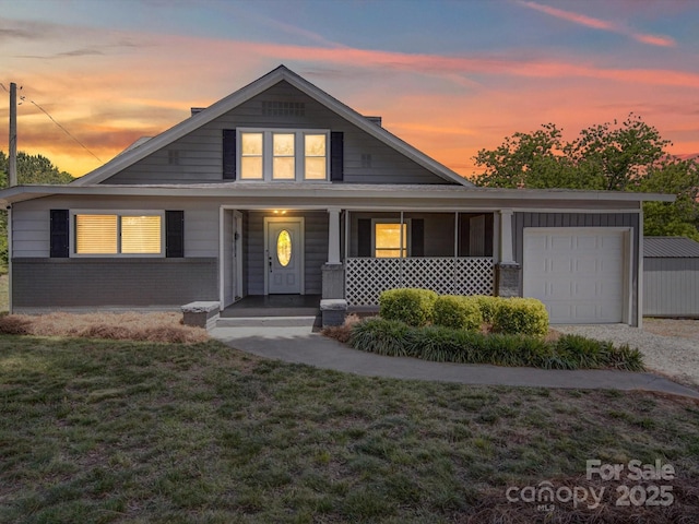 view of front of house with an attached garage, a front yard, a porch, driveway, and brick siding