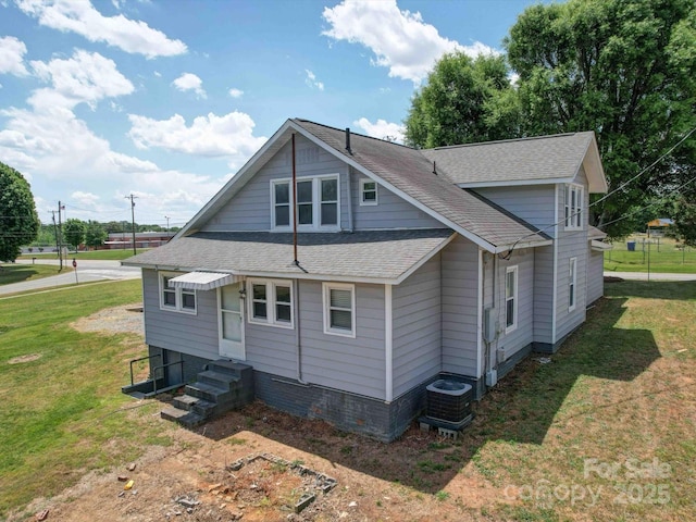 exterior space featuring central AC unit, entry steps, a front lawn, and a shingled roof