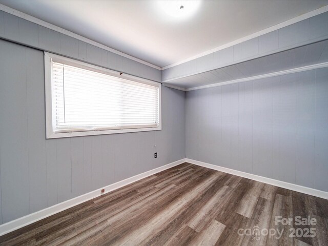 empty room featuring crown molding, wood finished floors, and baseboards