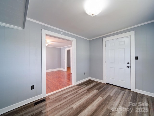 empty room with crown molding, baseboards, visible vents, and wood finished floors