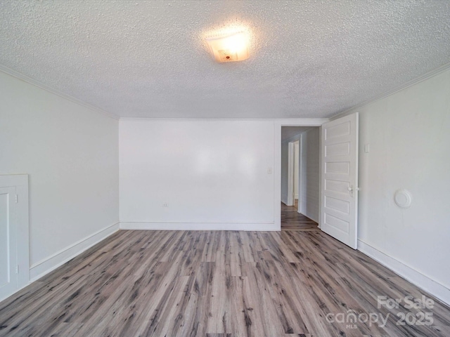 spare room with ornamental molding, a textured ceiling, baseboards, and wood finished floors