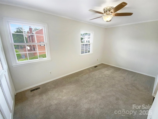 carpeted empty room featuring a ceiling fan, baseboards, visible vents, and ornamental molding