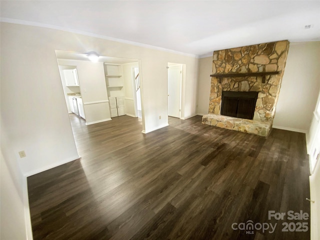unfurnished living room with crown molding, dark wood-style flooring, baseboards, and a stone fireplace