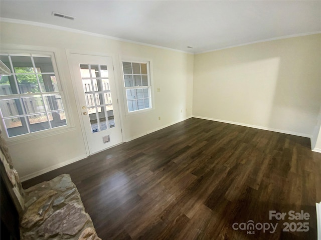 empty room featuring visible vents, dark wood finished floors, crown molding, and baseboards