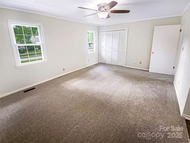 unfurnished bedroom featuring crown molding, carpet flooring, baseboards, visible vents, and a closet