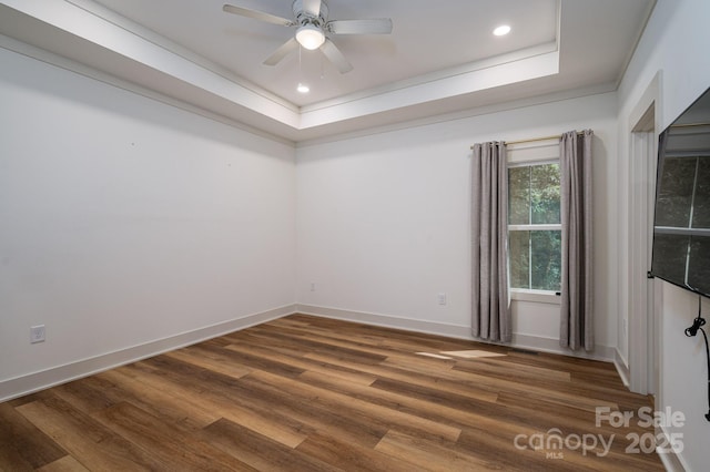 spare room featuring a raised ceiling, ceiling fan, baseboards, and wood finished floors