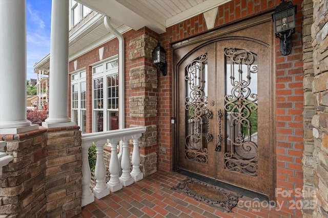 doorway to property with french doors, brick siding, and a porch