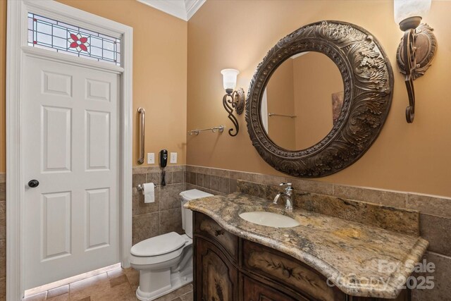 bathroom featuring tile walls, vanity, toilet, a wainscoted wall, and ornamental molding