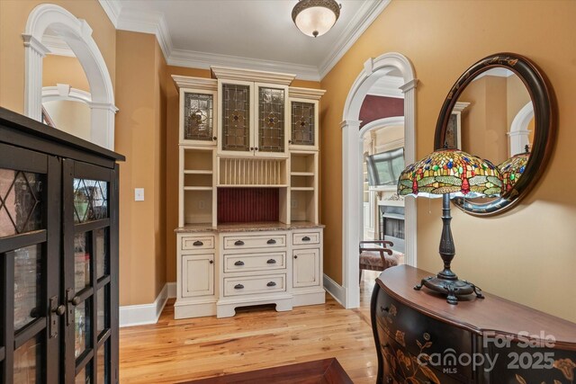 hallway featuring light wood-style floors, crown molding, and baseboards