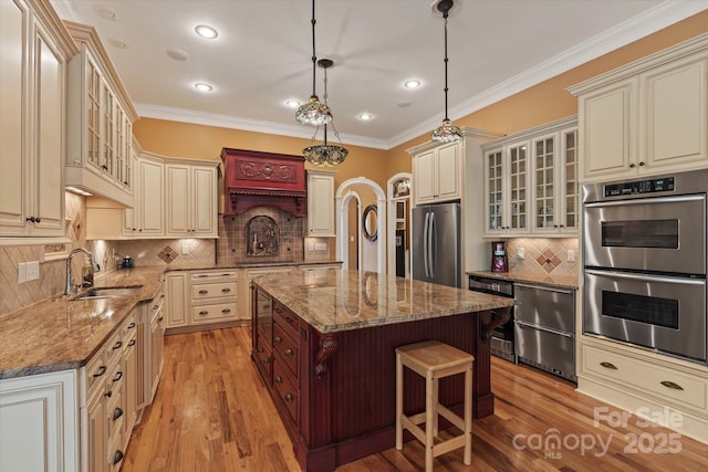 kitchen with stainless steel appliances, cream cabinets, a sink, backsplash, and light wood-type flooring
