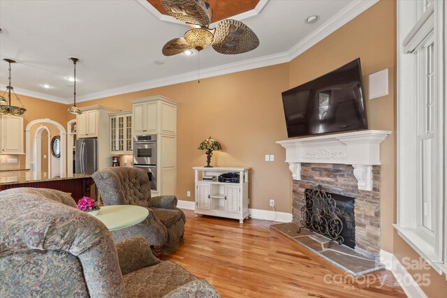 living room with ceiling fan, light wood-style floors, crown molding, a fireplace, and baseboards