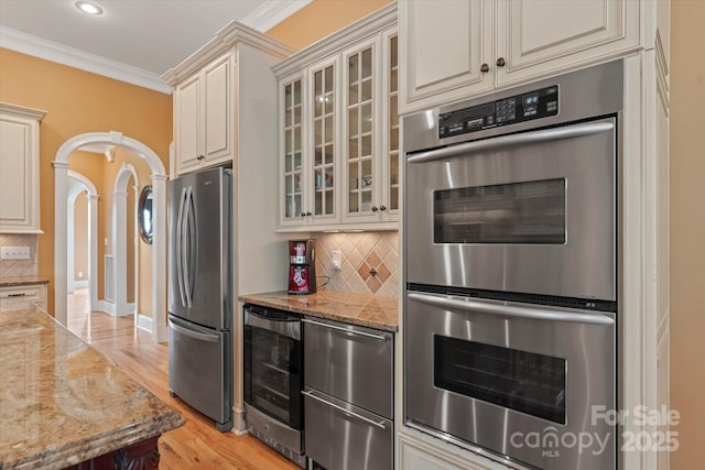 kitchen with cream cabinets, appliances with stainless steel finishes, beverage cooler, light wood-style floors, and crown molding