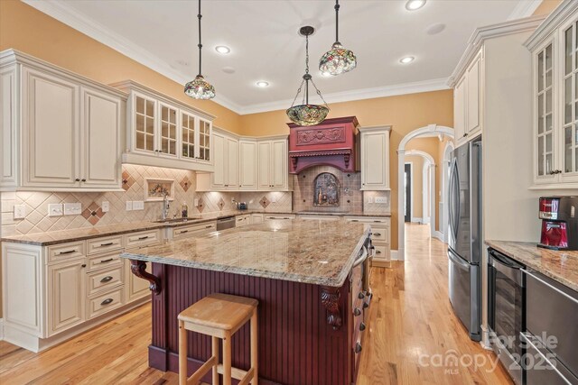 kitchen with a sink, appliances with stainless steel finishes, wine cooler, cream cabinets, and ornamental molding