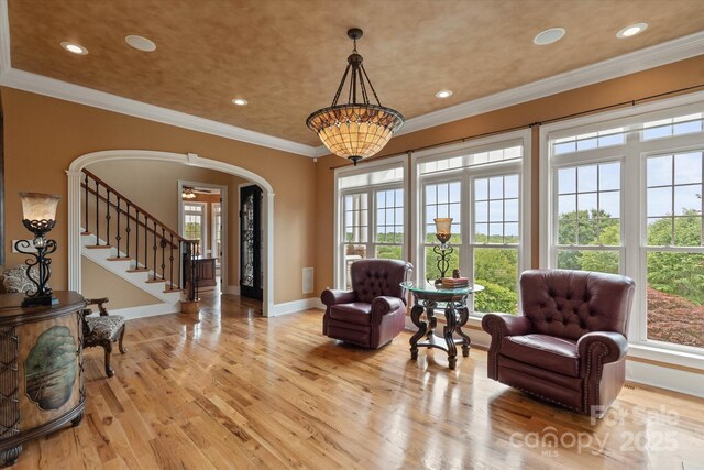 living area featuring arched walkways, wood finished floors, recessed lighting, baseboards, and crown molding