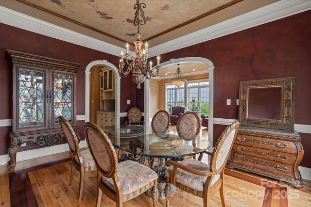 dining room featuring arched walkways, ornamental molding, wood finished floors, and a chandelier