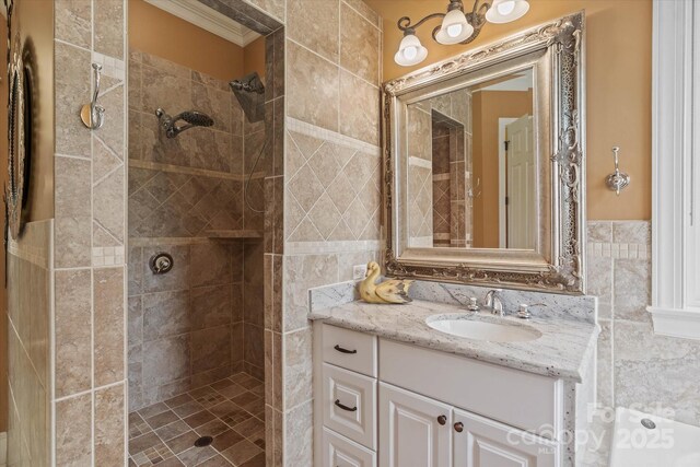 full bath featuring tile walls, a tile shower, vanity, and ornamental molding