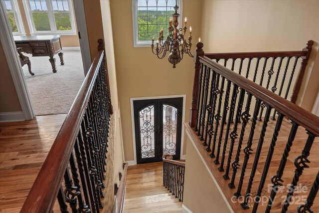 staircase with a chandelier, wood finished floors, french doors, and baseboards