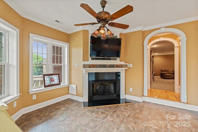 unfurnished living room featuring crown molding, a ceiling fan, a fireplace with raised hearth, arched walkways, and baseboards