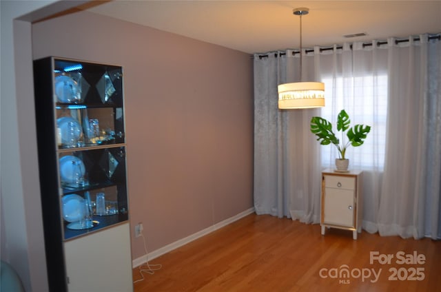 unfurnished dining area with baseboards, wood finished floors, and visible vents