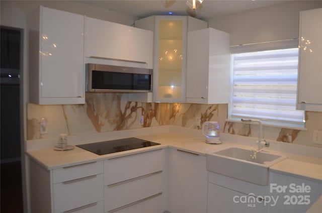 kitchen featuring white cabinetry, stainless steel microwave, a sink, and modern cabinets