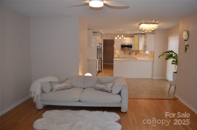 living room with baseboards, ceiling fan with notable chandelier, and light wood finished floors