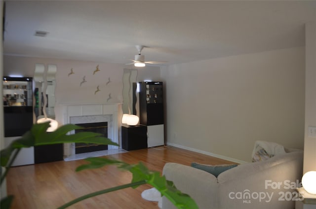living area featuring baseboards, ceiling fan, a fireplace, and wood finished floors