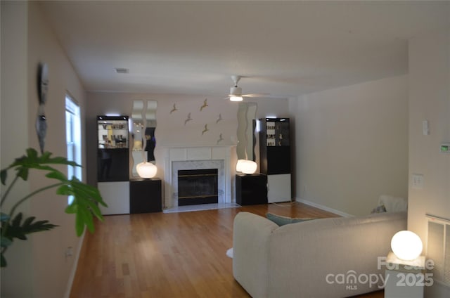 living room featuring baseboards, ceiling fan, a fireplace, and wood finished floors