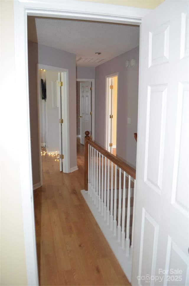 corridor featuring baseboards, light wood finished floors, and an upstairs landing