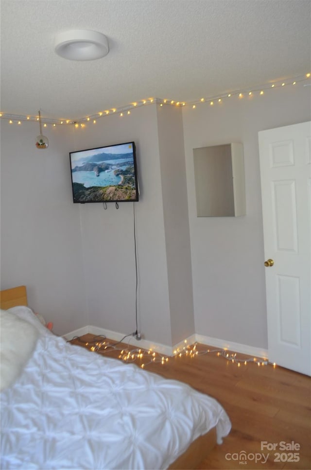 bedroom with baseboards, a textured ceiling, and wood finished floors