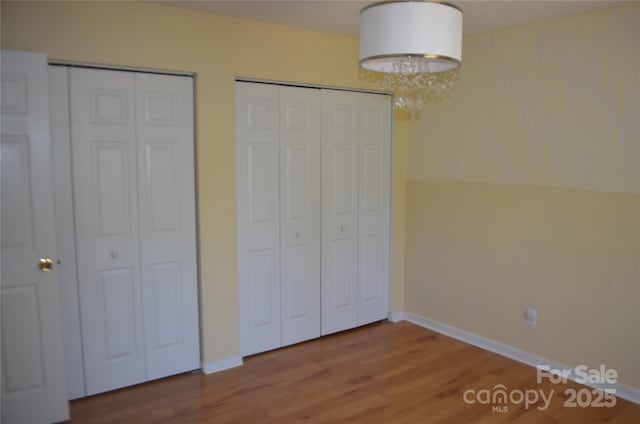 unfurnished bedroom featuring an inviting chandelier, baseboards, two closets, and wood finished floors