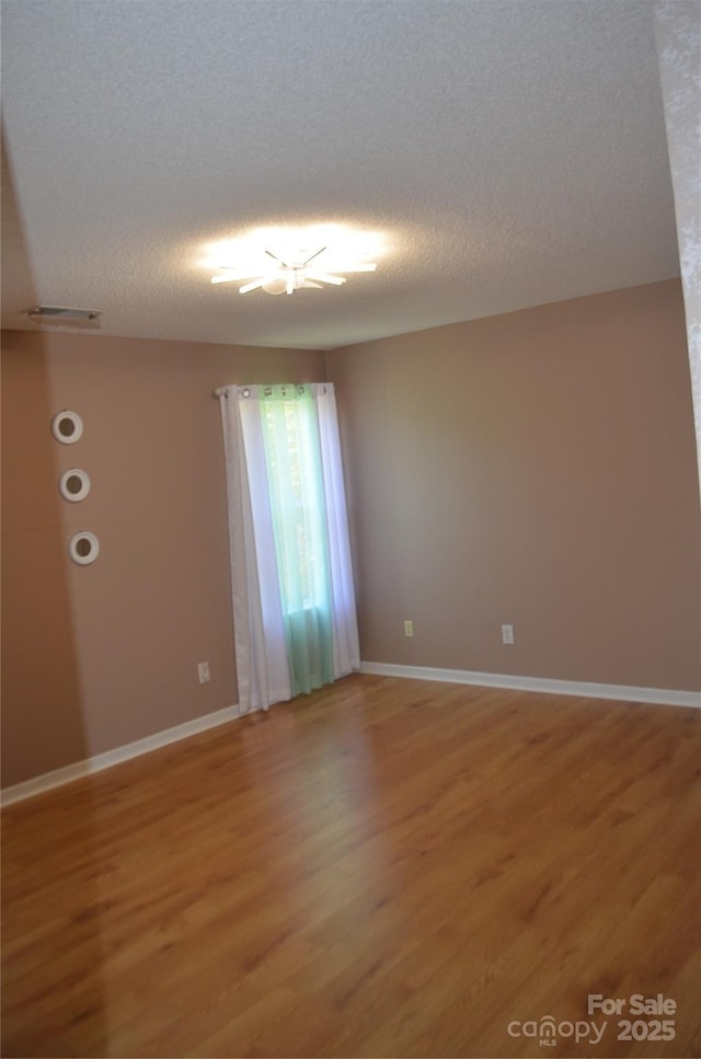 empty room with light wood-style floors, baseboards, a textured ceiling, and visible vents