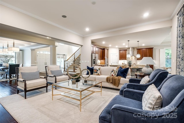 living room featuring hardwood / wood-style flooring, decorative columns, crown molding, recessed lighting, and stairs