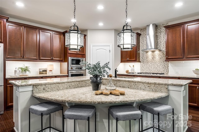 kitchen featuring wall chimney range hood, stainless steel appliances, a sink, an island with sink, and dark wood-style flooring