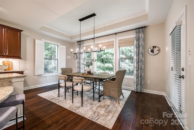 dining area featuring a tray ceiling, dark wood-style flooring, baseboards, ornamental molding, and a chandelier